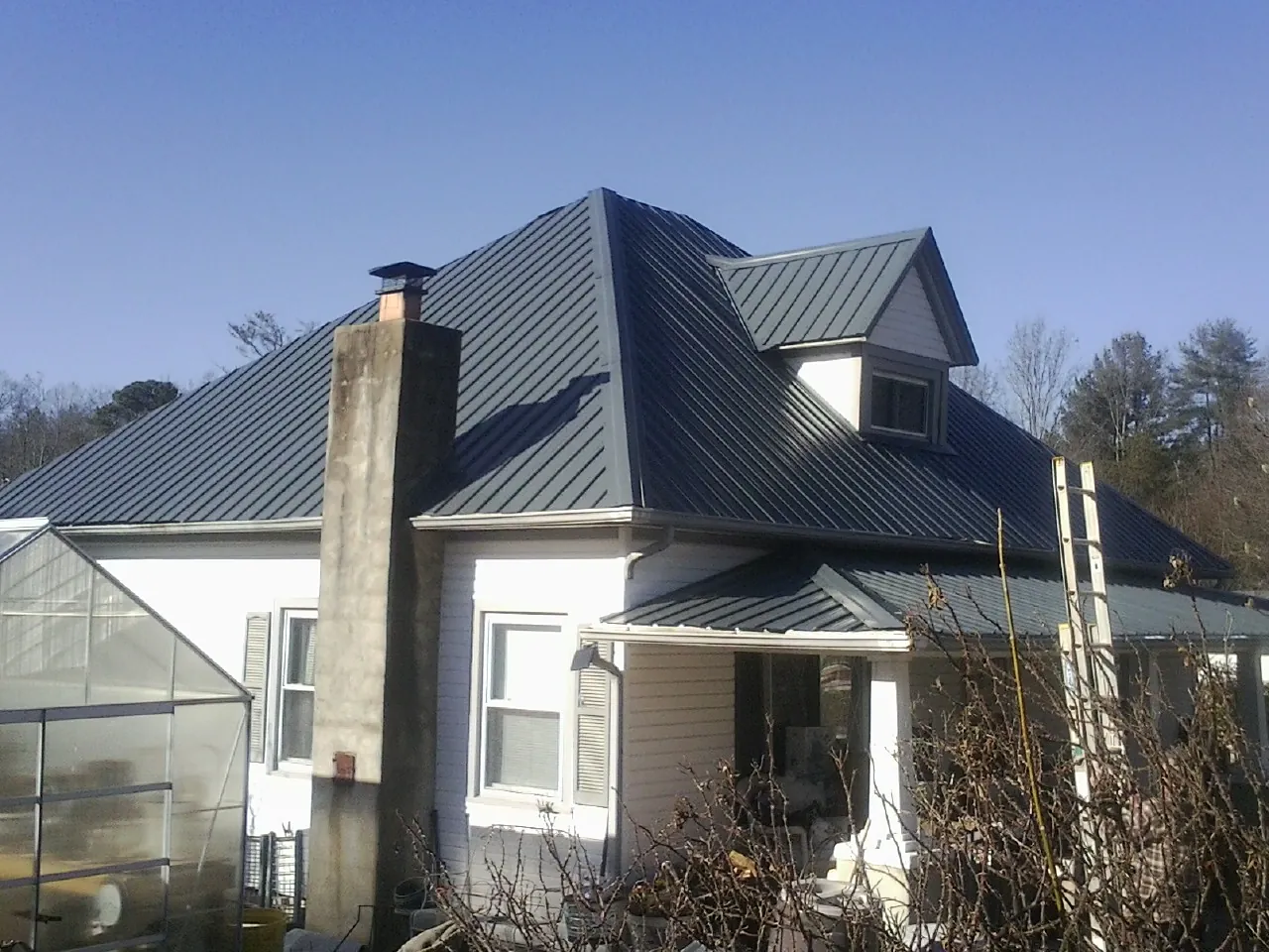 Dark blue standing seam metal roof on a white farmhouse with dormer — Slate & Tile Roof Repair by Roofing Brothers in New Waterford