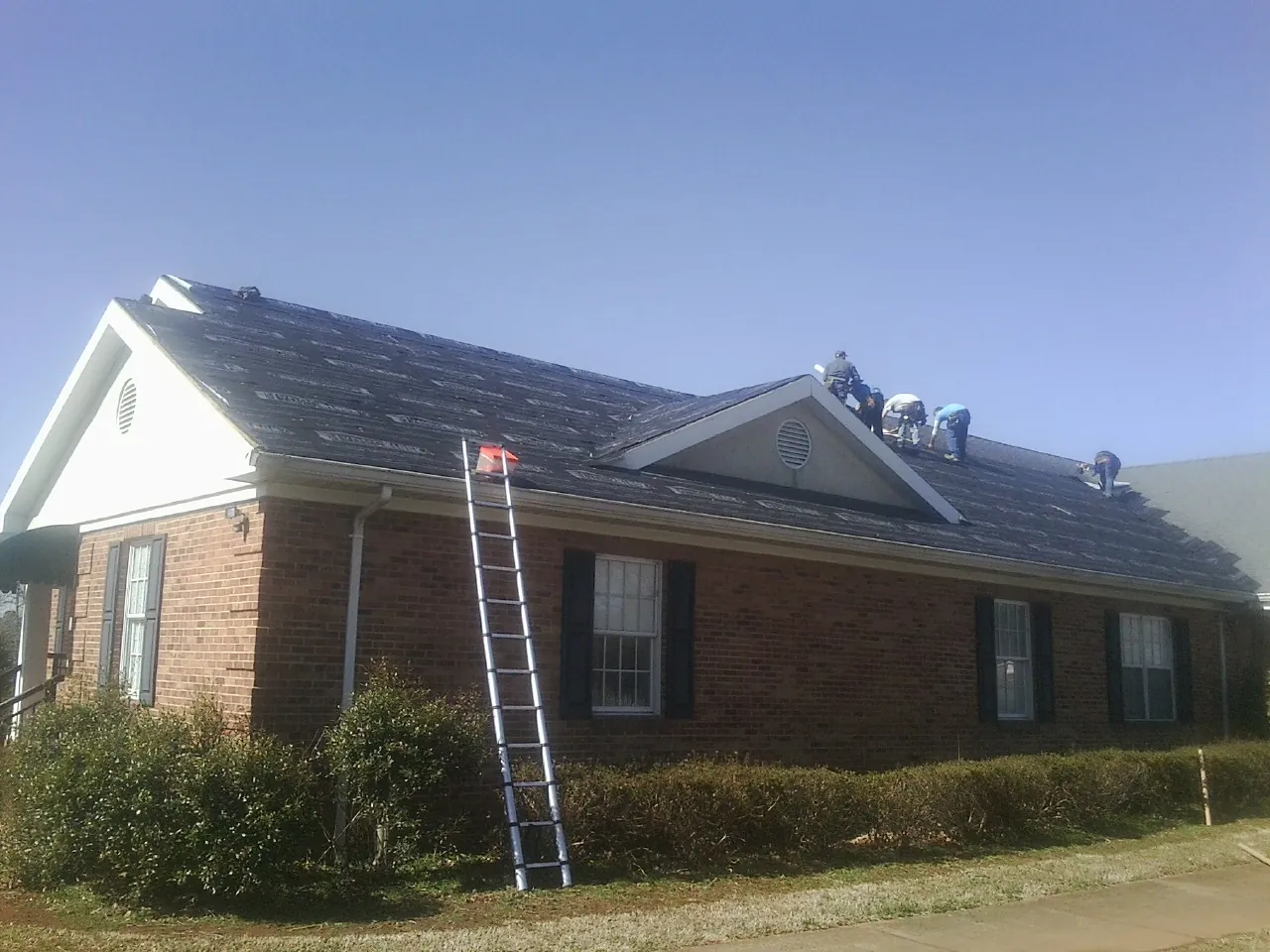 Crew tearing shingles off a brick ranch roof with a ladder set — Metal Roof Repair work by our crew in New Waterford