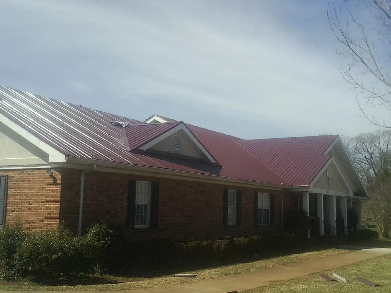 Red metal roof with gabled entries on a long brick building, from a Hail Damage Roof Repair job in New Waterford