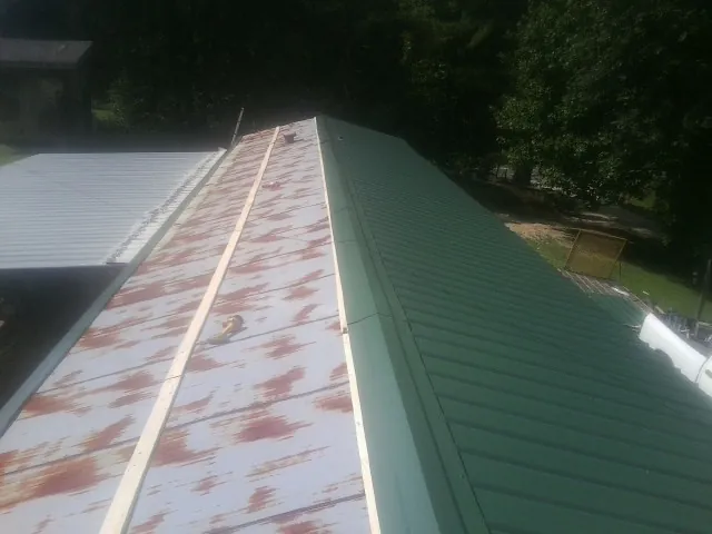 Old rusted panels beside newly installed green metal roofing — Wind Damage Roof Repair by Roofing Brothers in New Waterford