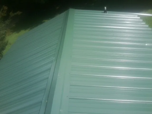 New green metal panels meeting at the ridge of a roof — Flat Roof Repair work by our crew in New Waterford