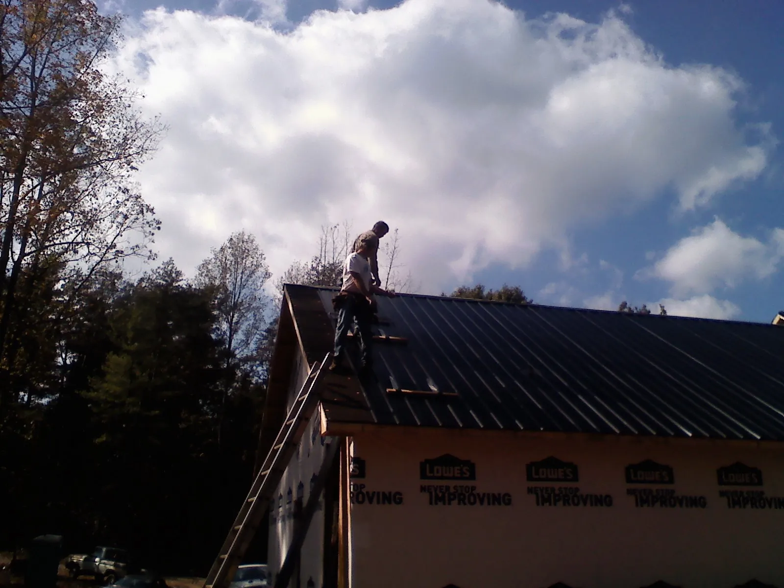 Roofer fastening dark metal panels high against a cloudy sky, from a Roof Inspection job in New Waterford