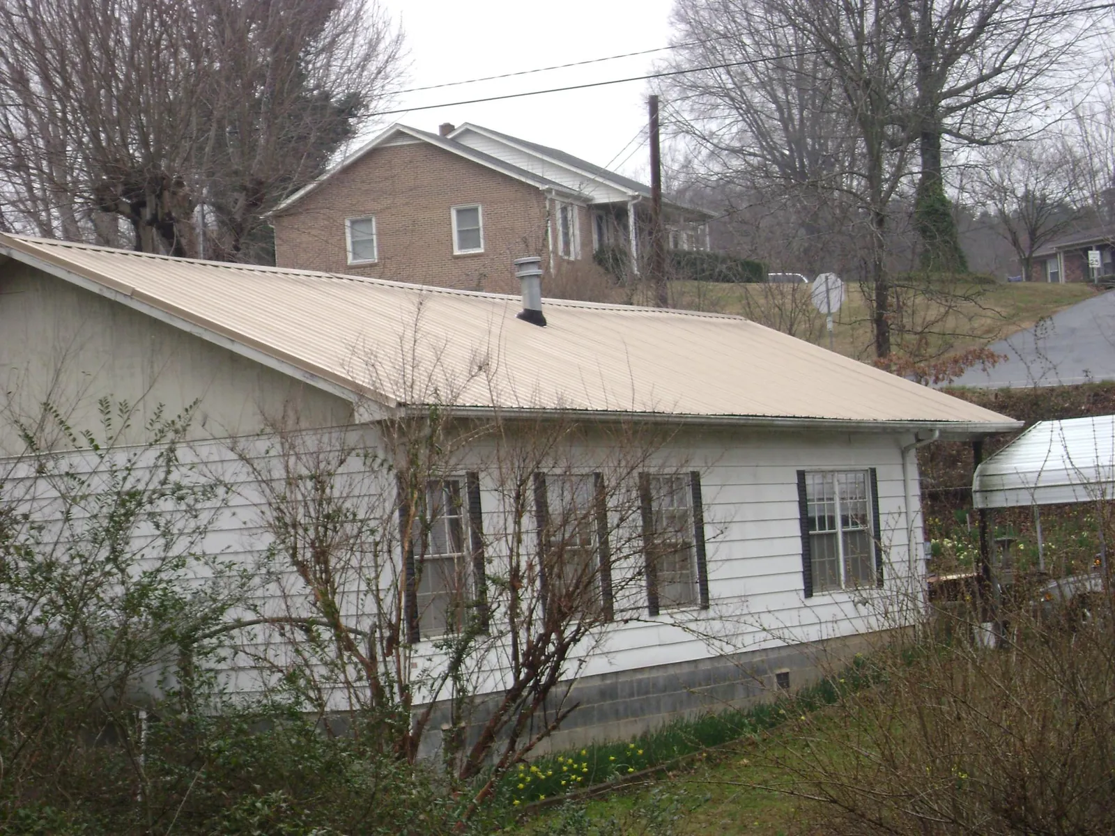 Tan metal roof on a white sided house set into a hillside — Commercial Roofing by Roofing Brothers in New Waterford